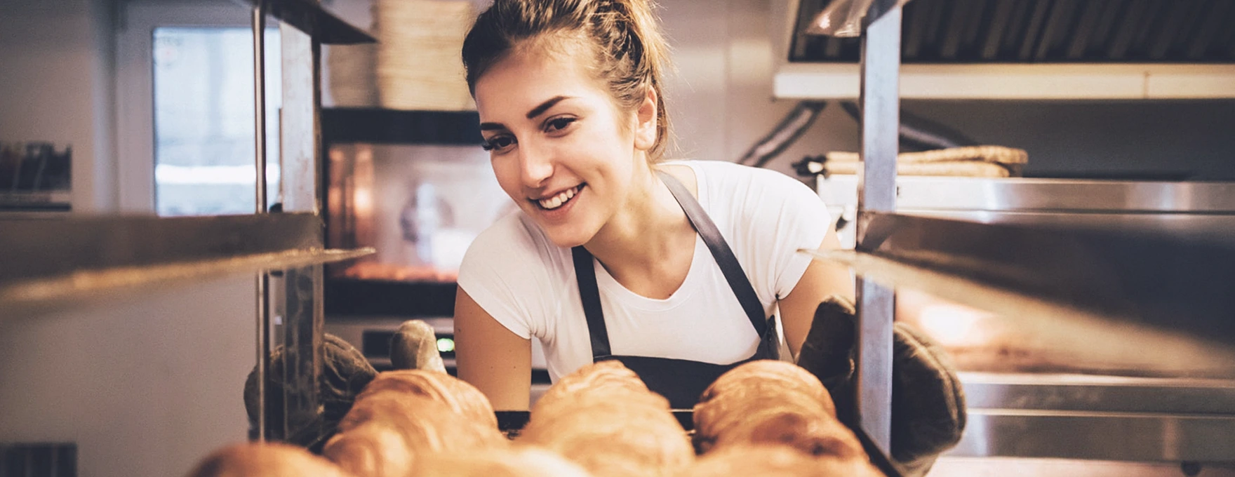 Mulher jovem sorridente verificando bandeja de pães tipo croissant.