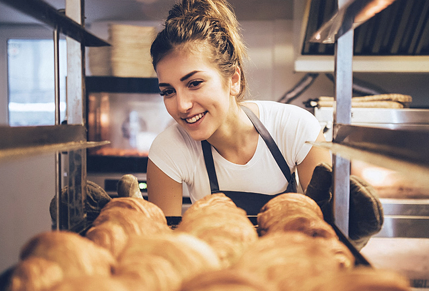 Mulher jovem sorridente verificando bandeja de pães tipo croissant.